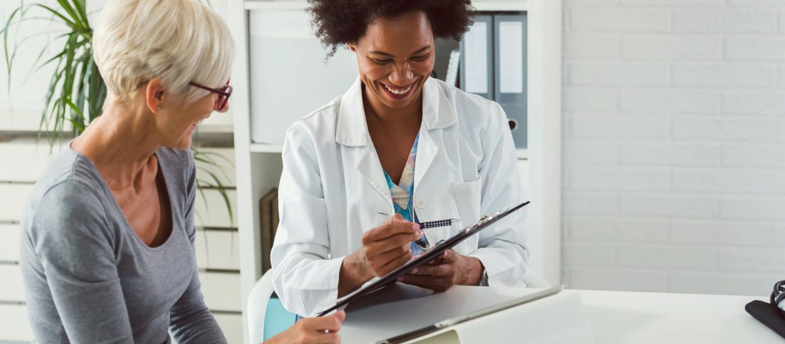 A female doctor sits at her desk and chats to an elderly female