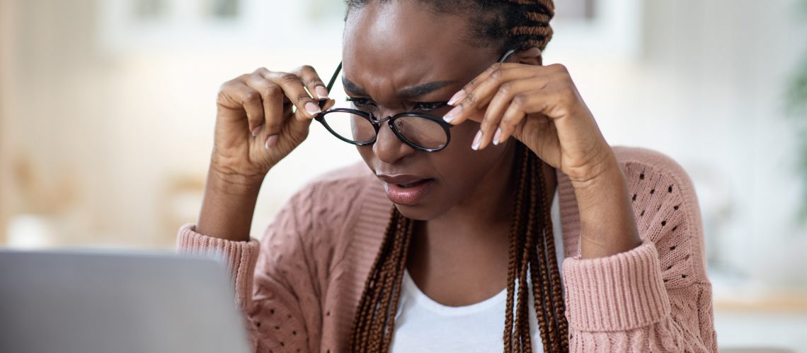 Eyesight Problems. Black Lady In Glasses Squinting While Looking At Laptop Screen, Millennial Freelancer Lady Having Eye Vision Troubles While Working Remotely With Computer At Home, Closeup